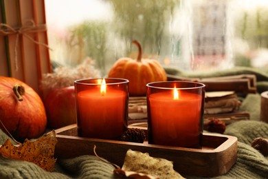 Photo of Burning candles and autumn decor on green sweater near window