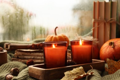 Photo of Burning candles and autumn decor on green sweater near window