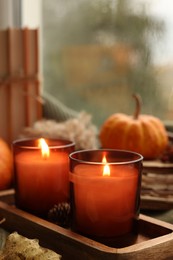 Photo of Burning candles and autumn decor on table near window, closeup