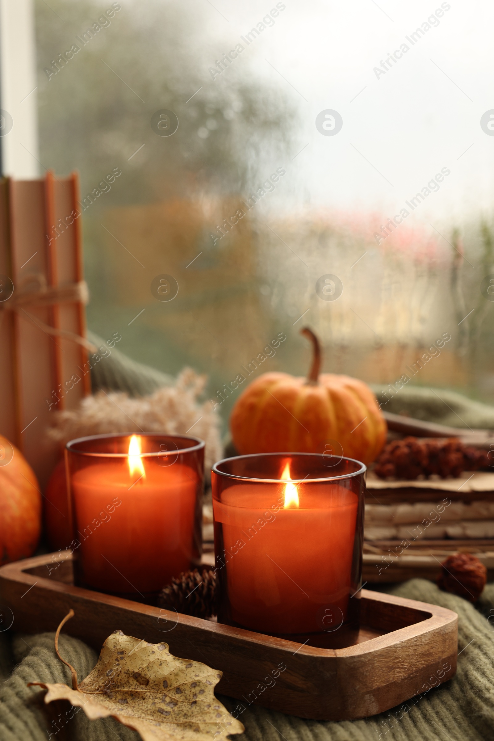 Photo of Burning candles and autumn decor on green sweater near window