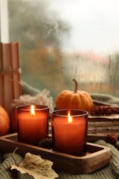 Photo of Burning candles and autumn decor on green sweater near window