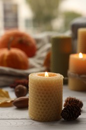 Photo of Autumn atmosphere. Burning candle and pinecones on grey wooden table, closeup