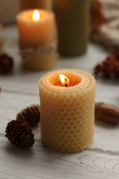 Photo of Autumn atmosphere. Burning candle, pinecones and acorn on grey wooden table, closeup