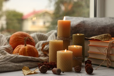 Photo of Burning candles, books, sweaters and autumn decor on grey wooden table near window