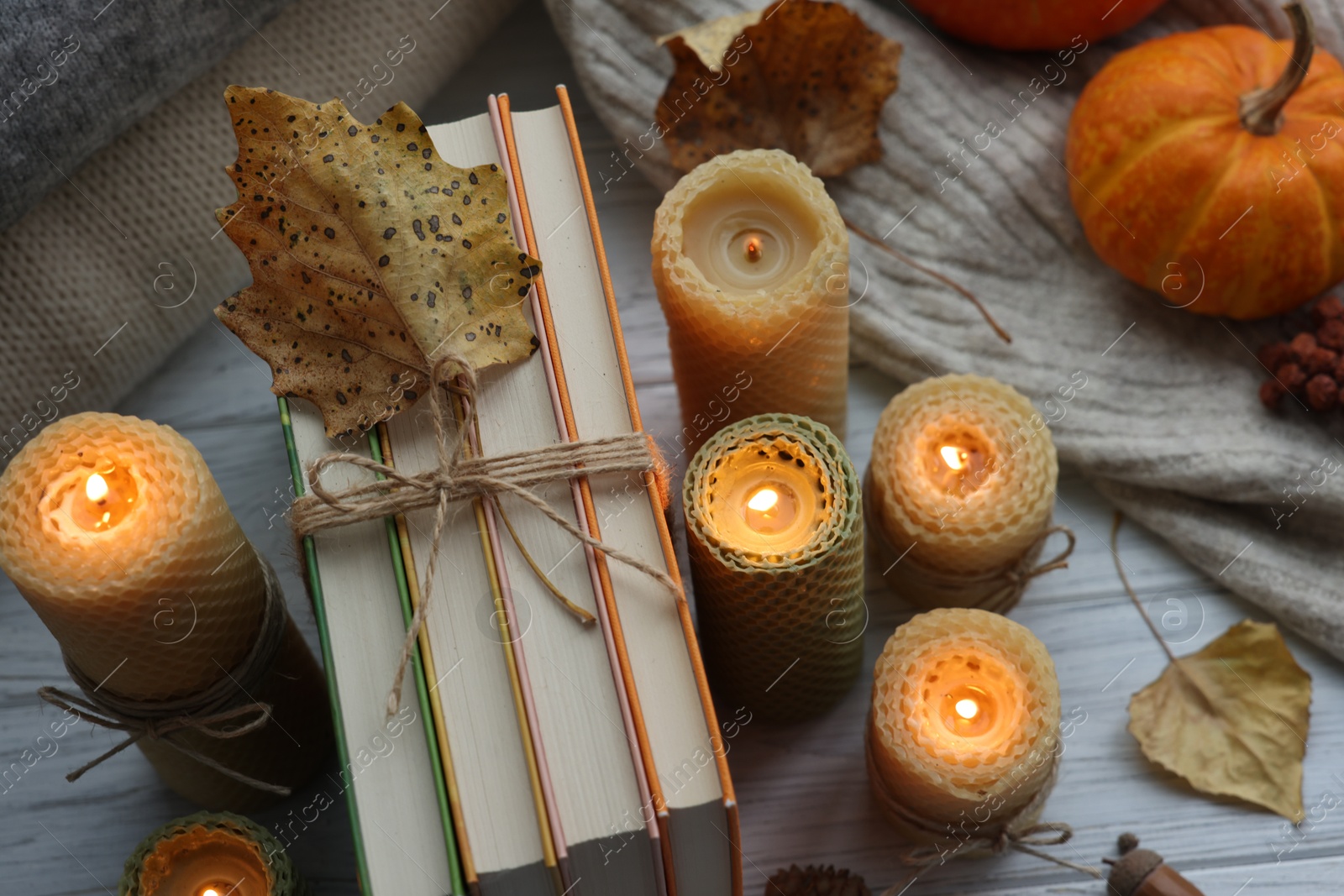 Photo of Burning candles, books, sweaters and autumn decor on grey wooden table, closeup