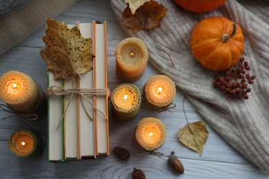 Photo of Burning candles, books, sweaters and autumn decor on grey wooden table, flat lay