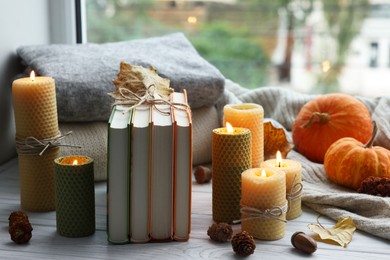 Photo of Burning candles, books, sweaters and autumn decor on grey wooden table near window