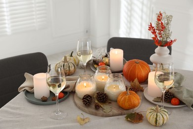 Photo of Autumn place setting with burning candles, glasses of wine and decor on table indoors