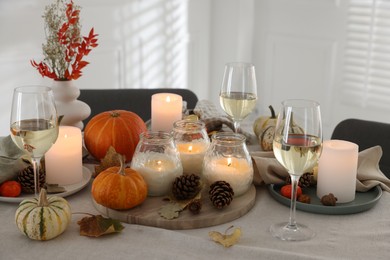 Photo of Autumn place setting with burning candles, glasses of wine and decor on table indoors