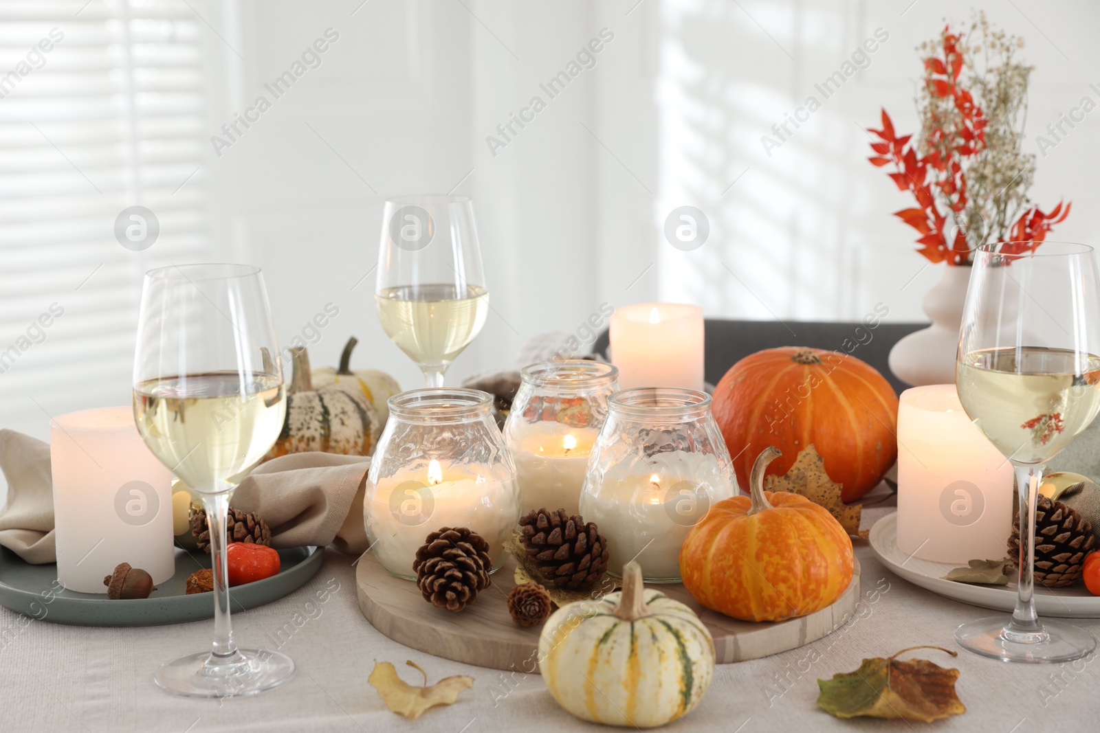 Photo of Autumn place setting with burning candles, glasses of wine and decor on table indoors