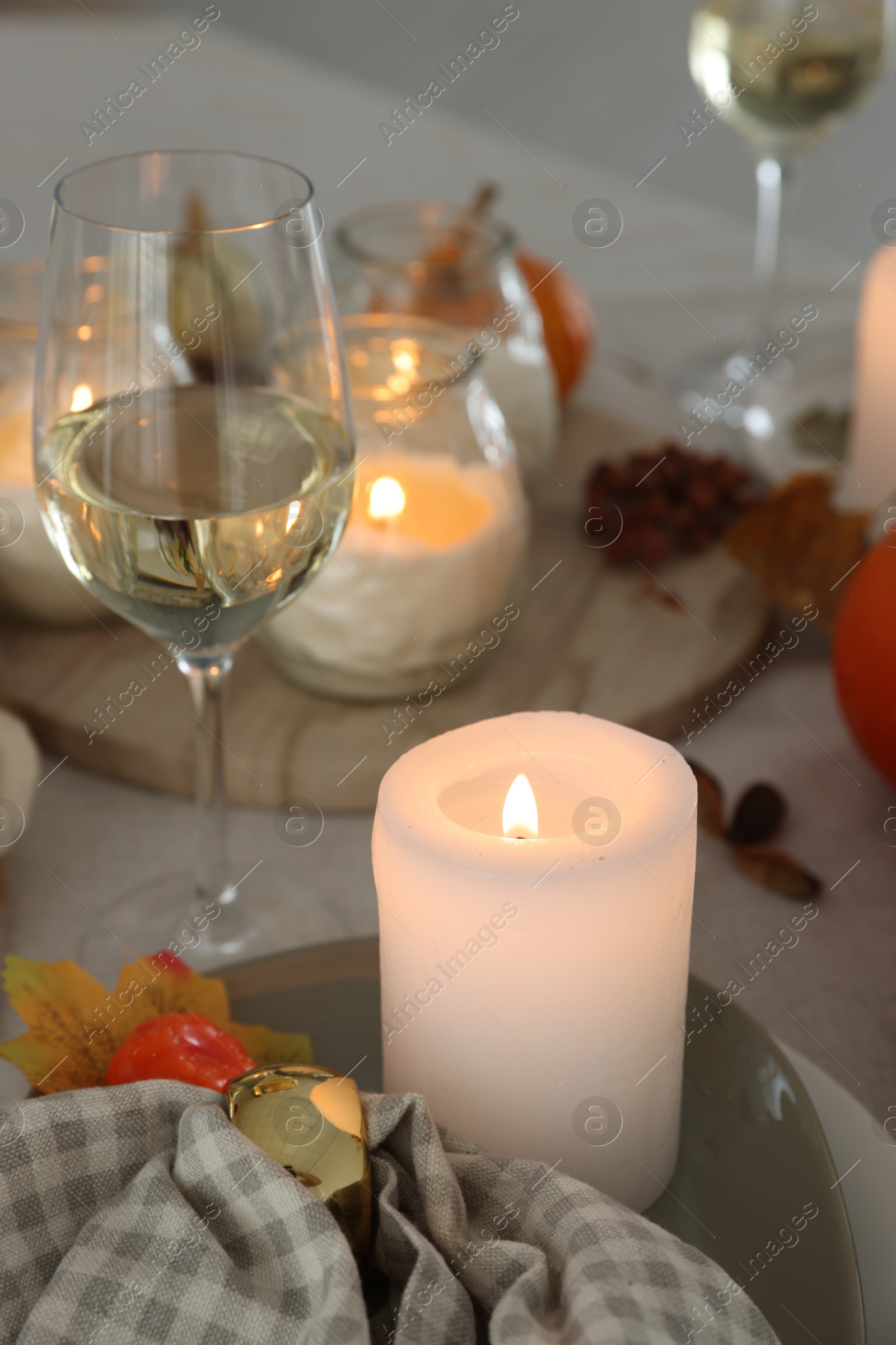 Photo of Burning candles, glass of wine and autumn decor on table, closeup