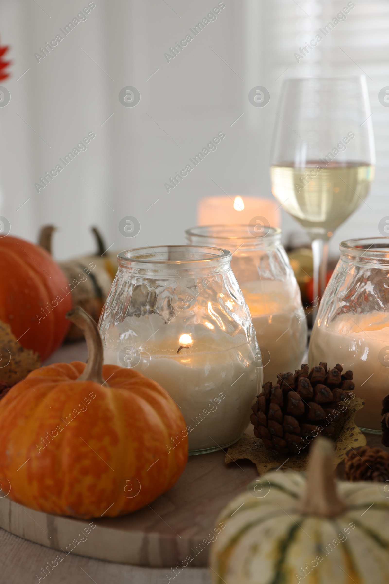 Photo of Burning candles, glass of wine and autumn decor on table, closeup