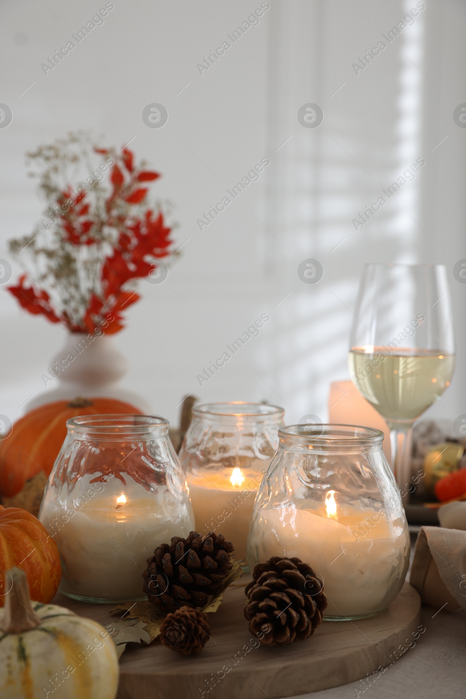 Photo of Burning candles, glass of wine and autumn decor on table, closeup