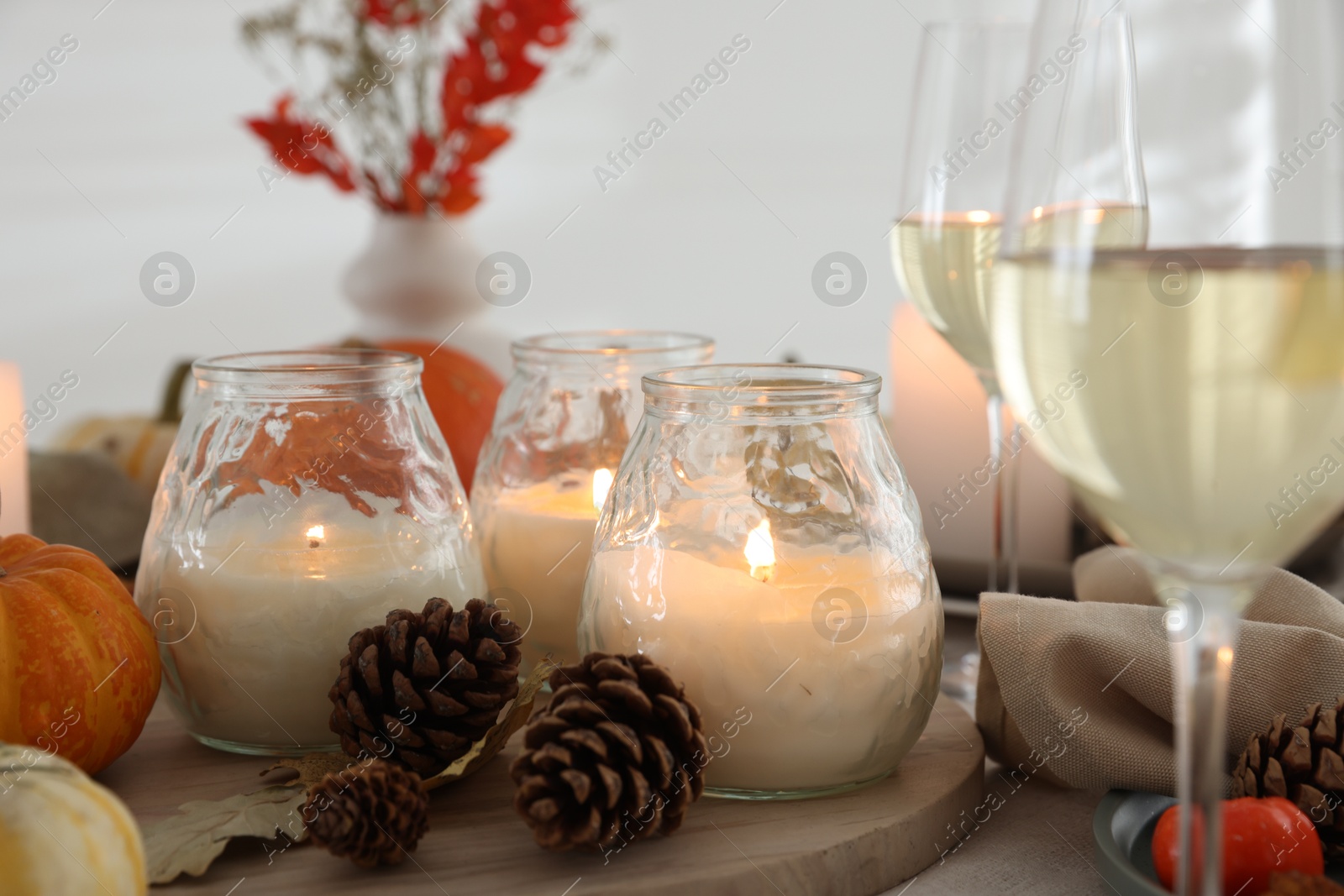 Photo of Burning candles, glasses of wine and autumn decor on table, closeup