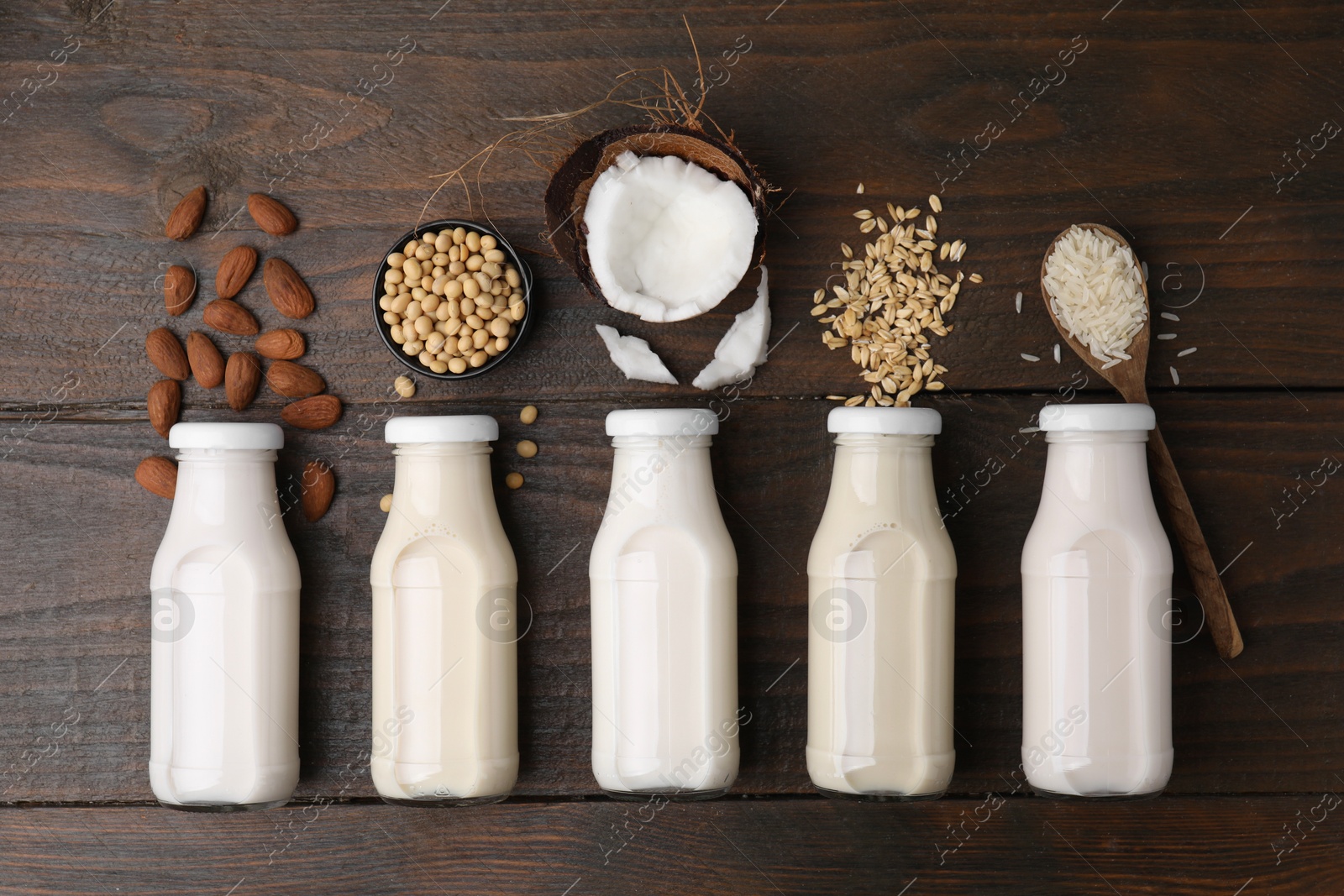 Photo of Different types of vegan milk in bottles and ingredients on wooden table, flat lay