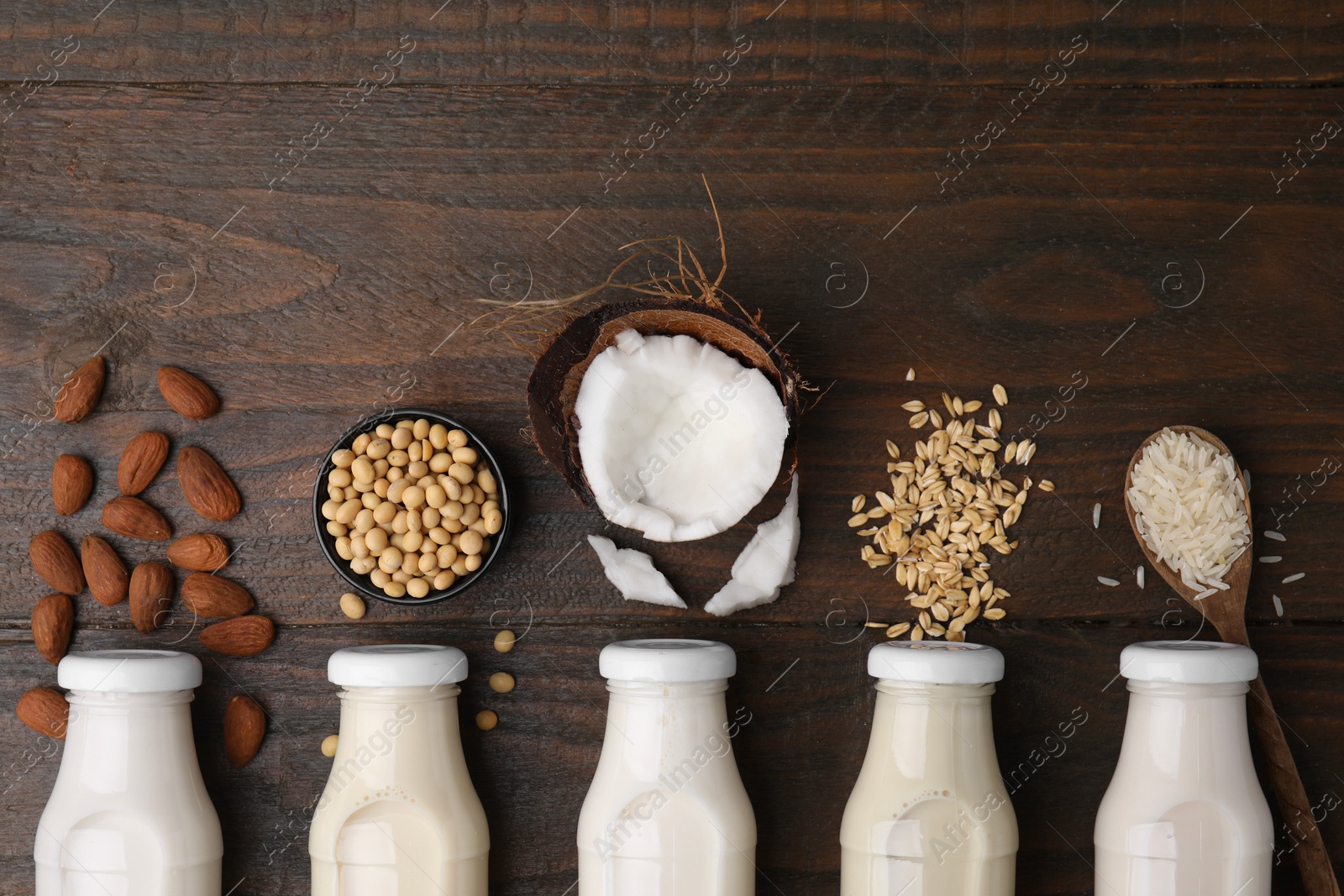 Photo of Different types of vegan milk in bottles and ingredients on wooden table, flat lay