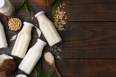 Photo of Different types of vegan milk in bottles with ingredients and leaves on wooden table, flat lay. Space for text