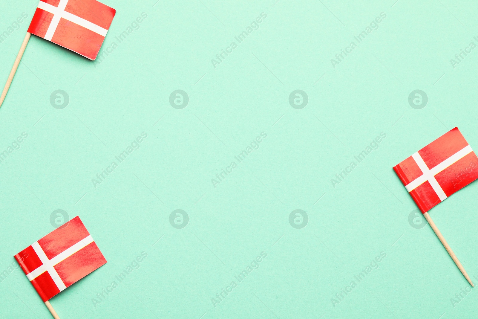 Photo of Small paper flags of Denmark on turquoise background, top view. Space for text