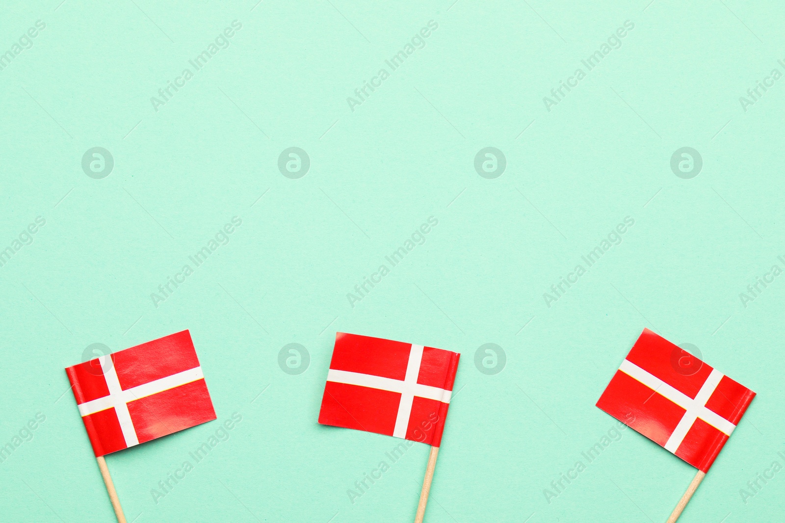 Photo of Small paper flags of Denmark on turquoise background, top view. Space for text