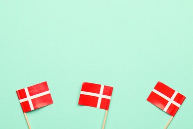 Photo of Small paper flags of Denmark on turquoise background, top view. Space for text