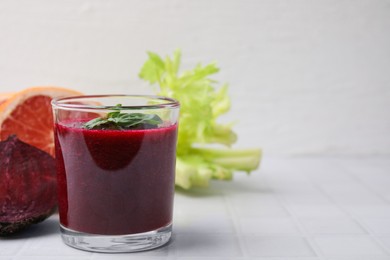 Photo of Vegan drink. Tasty beetroot smoothie in glass, fresh vegetables and grapefruit on white tiled table, closeup. Space for text