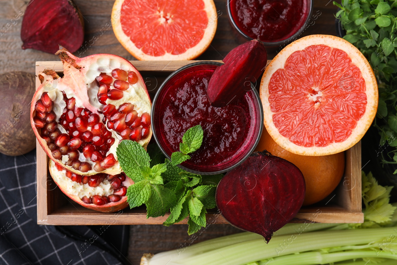 Photo of Glass of tasty beetroot smoothie, fresh vegetables, fruits and mint in wooden box on table, top view. Vegan drink