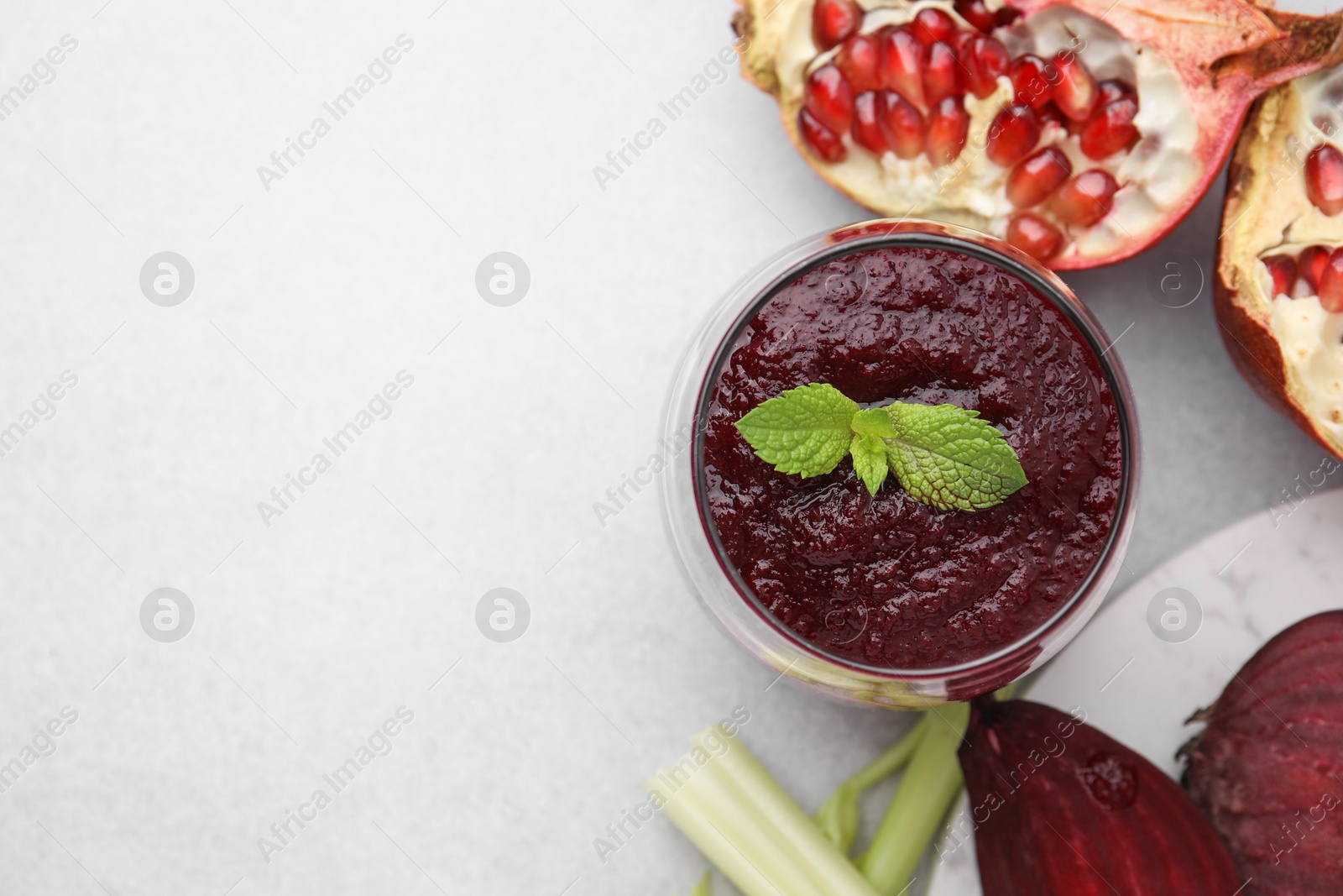 Photo of Tasty beetroot smoothie in glass, fresh vegetables and pomegranate on light table, flat lay with space for text. Vegan drink