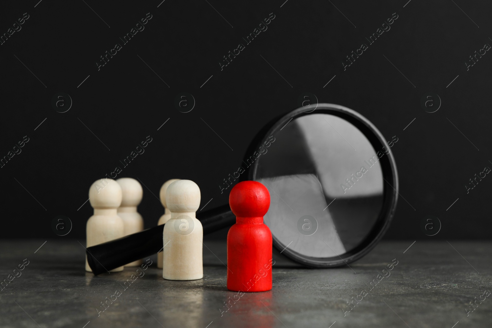 Photo of Red piece among wooden ones and magnifying glass on grey table