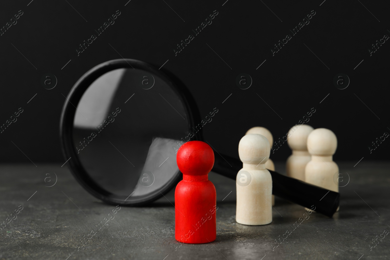 Photo of Red piece among wooden ones and magnifying glass on grey table