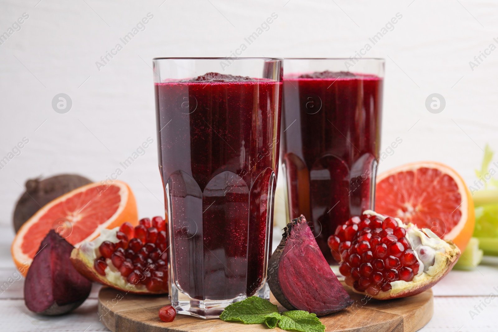 Photo of Fresh beetroot smoothie in glasses, grapefruit, beet and pomegranate on white wooden table