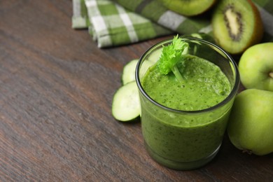 Photo of Tasty green smoothie in glass and cut cucumber on wooden table, closeup. Space for text