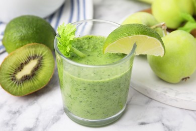 Photo of Tasty green smoothie in glass with lime and products on white marble table, closeup