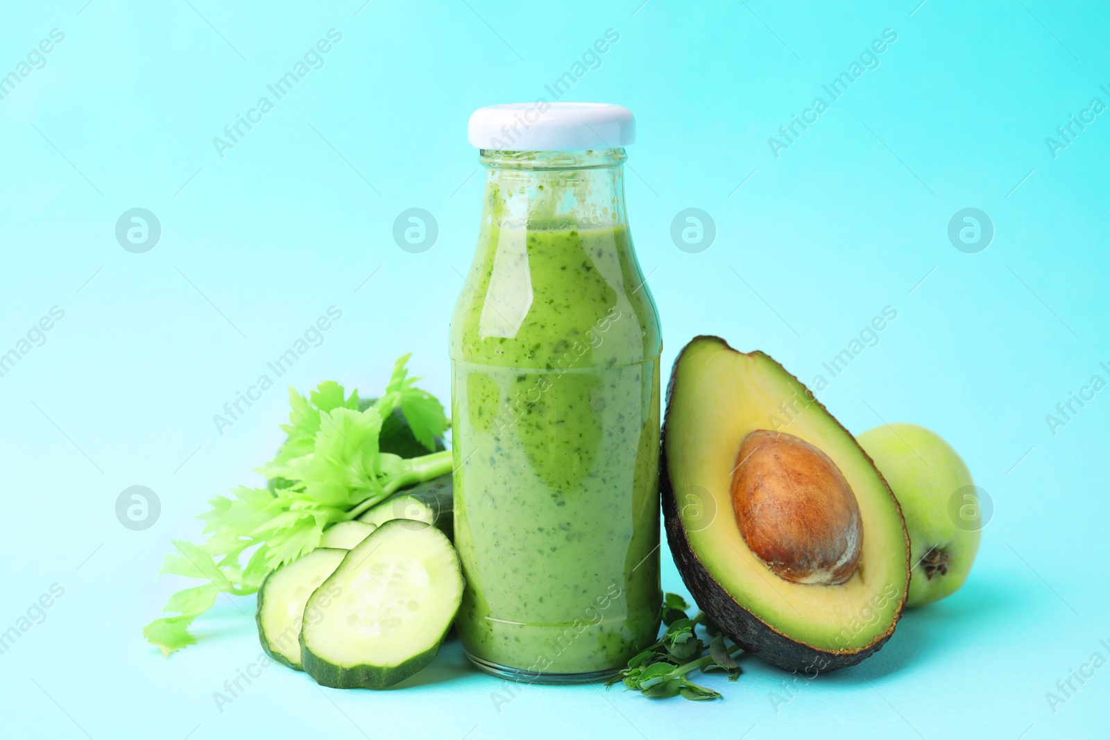 Photo of Tasty green smoothie in bottle and products on light blue background