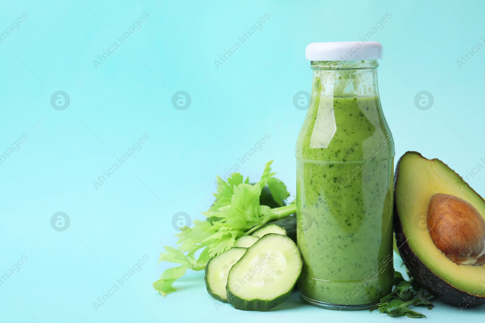 Photo of Tasty green smoothie in bottle and products on light blue background, closeup. Space for text