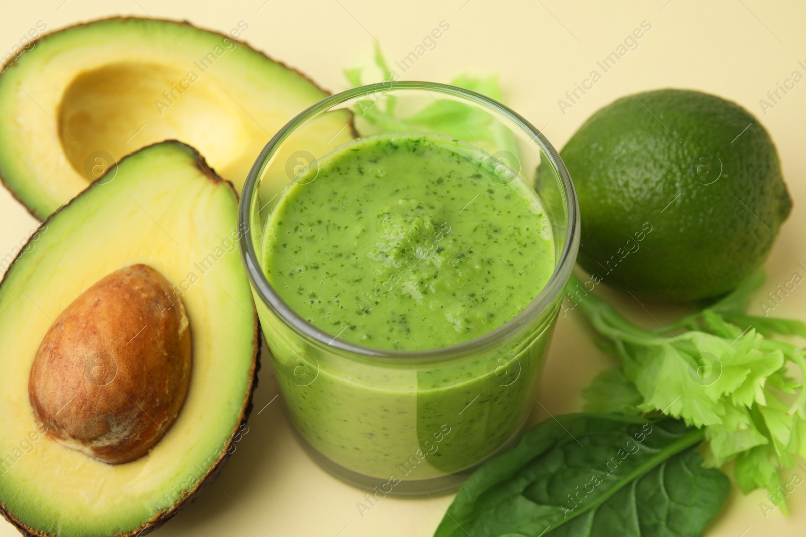 Photo of Tasty green smoothie in glass and products on beige background, closeup