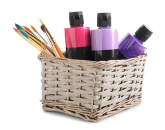 Photo of Acrylic paints of different colors and brushes in wicker basket isolated on white