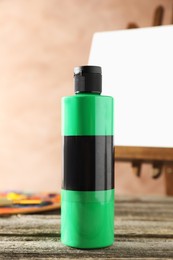 Photo of Green acrylic paint in bottle on wooden table