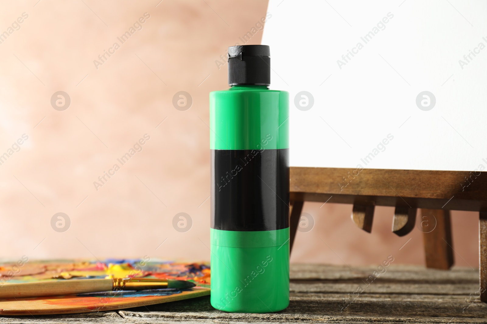 Photo of Green acrylic paint in bottle on wooden table