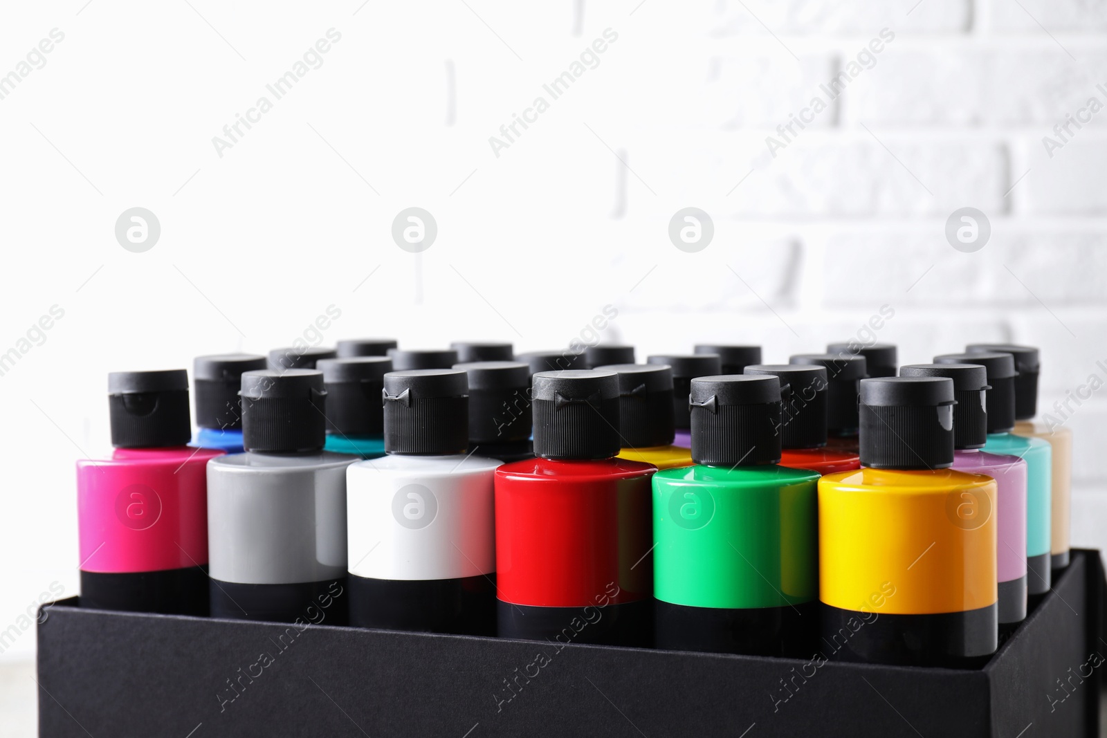 Photo of Acrylic paints of different colors in bottles against white brick wall