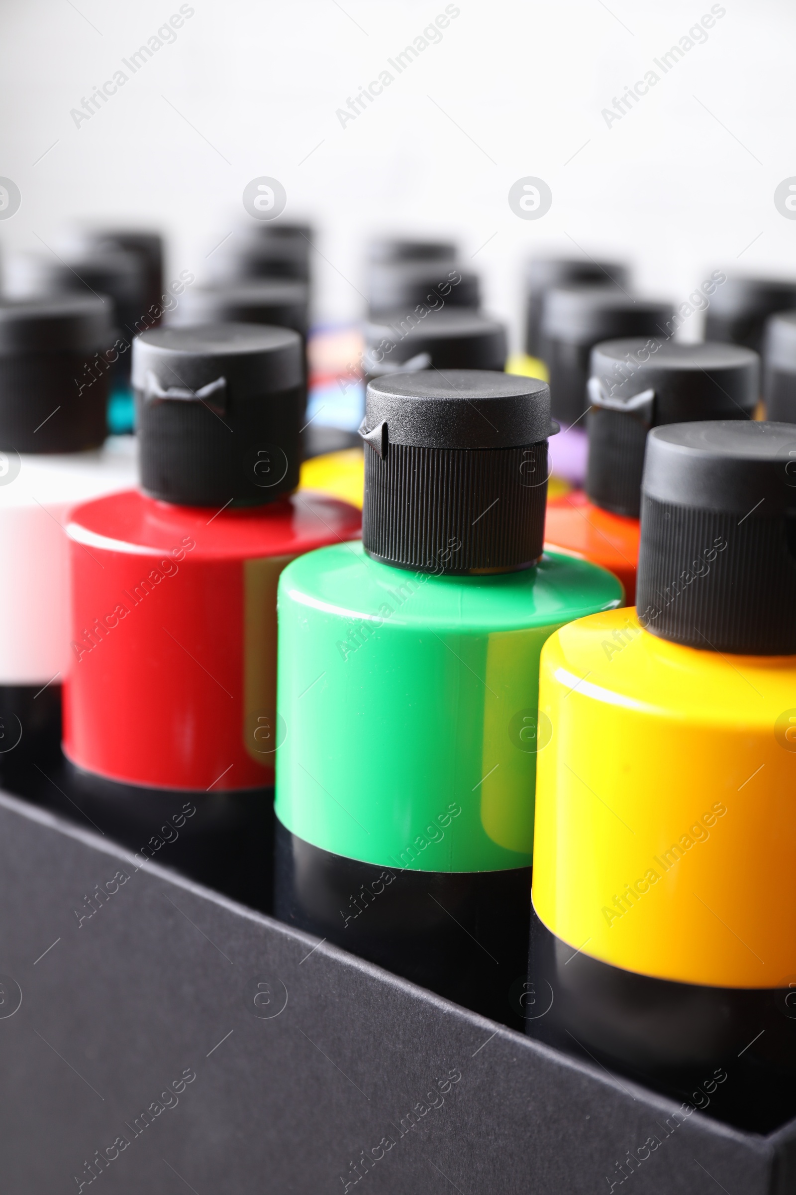 Photo of Acrylic paints of different colors in bottles against white background, closeup