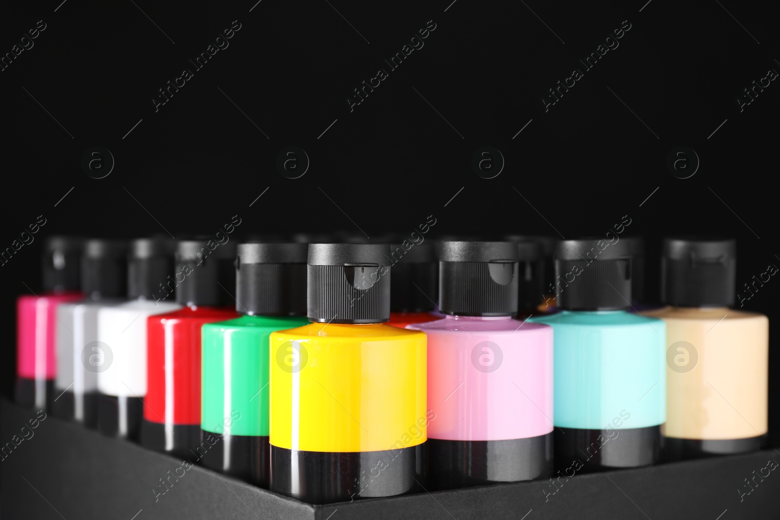 Photo of Acrylic paints of different colors in bottles against black background, closeup