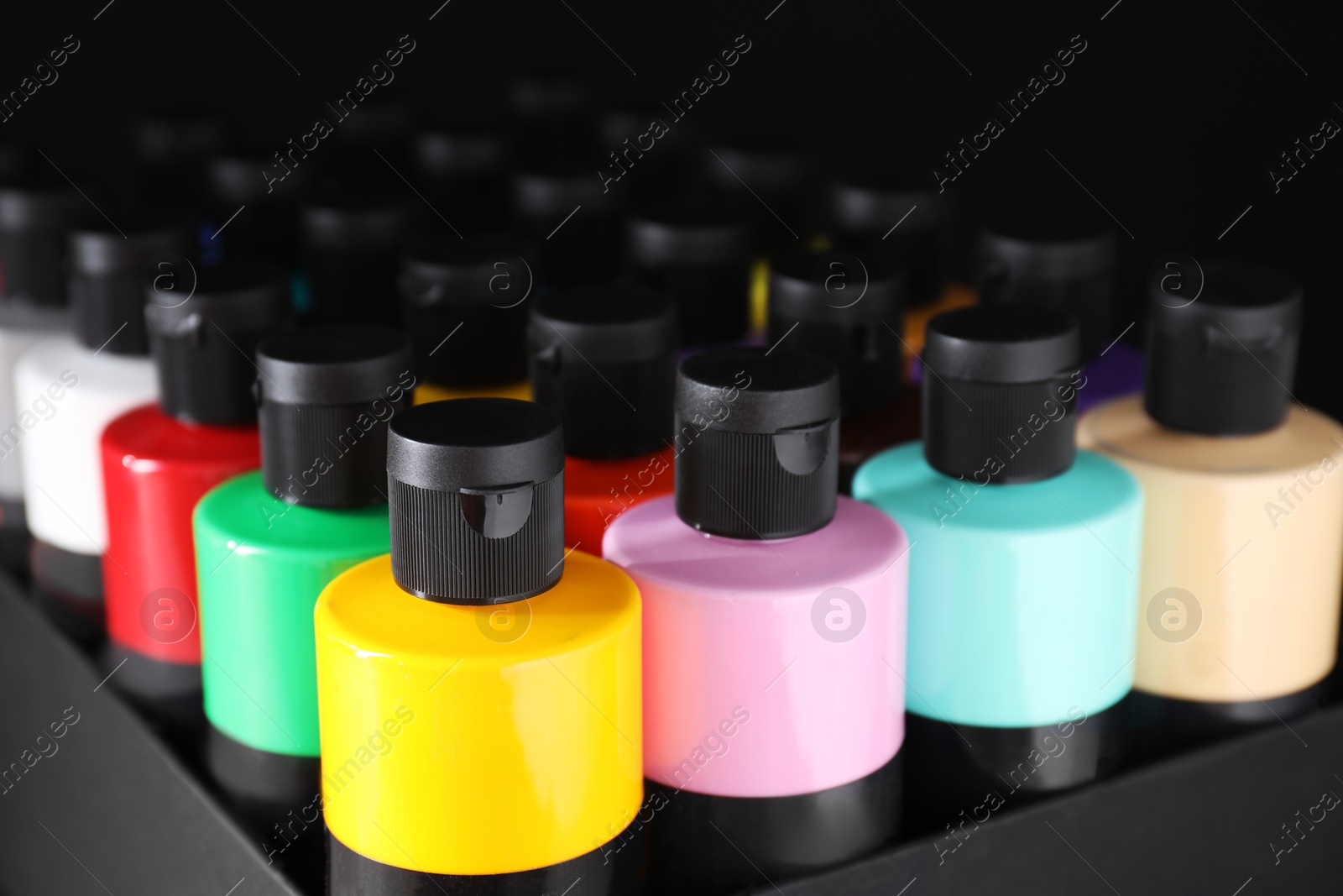 Photo of Acrylic paints of different colors in bottles against black background, closeup