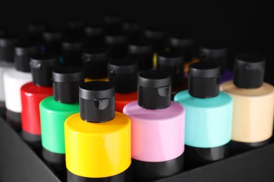 Photo of Acrylic paints of different colors in bottles against black background, closeup