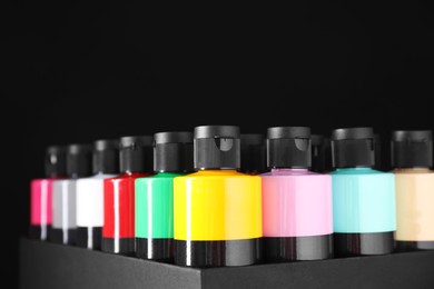 Photo of Acrylic paints of different colors in bottles against black background, closeup