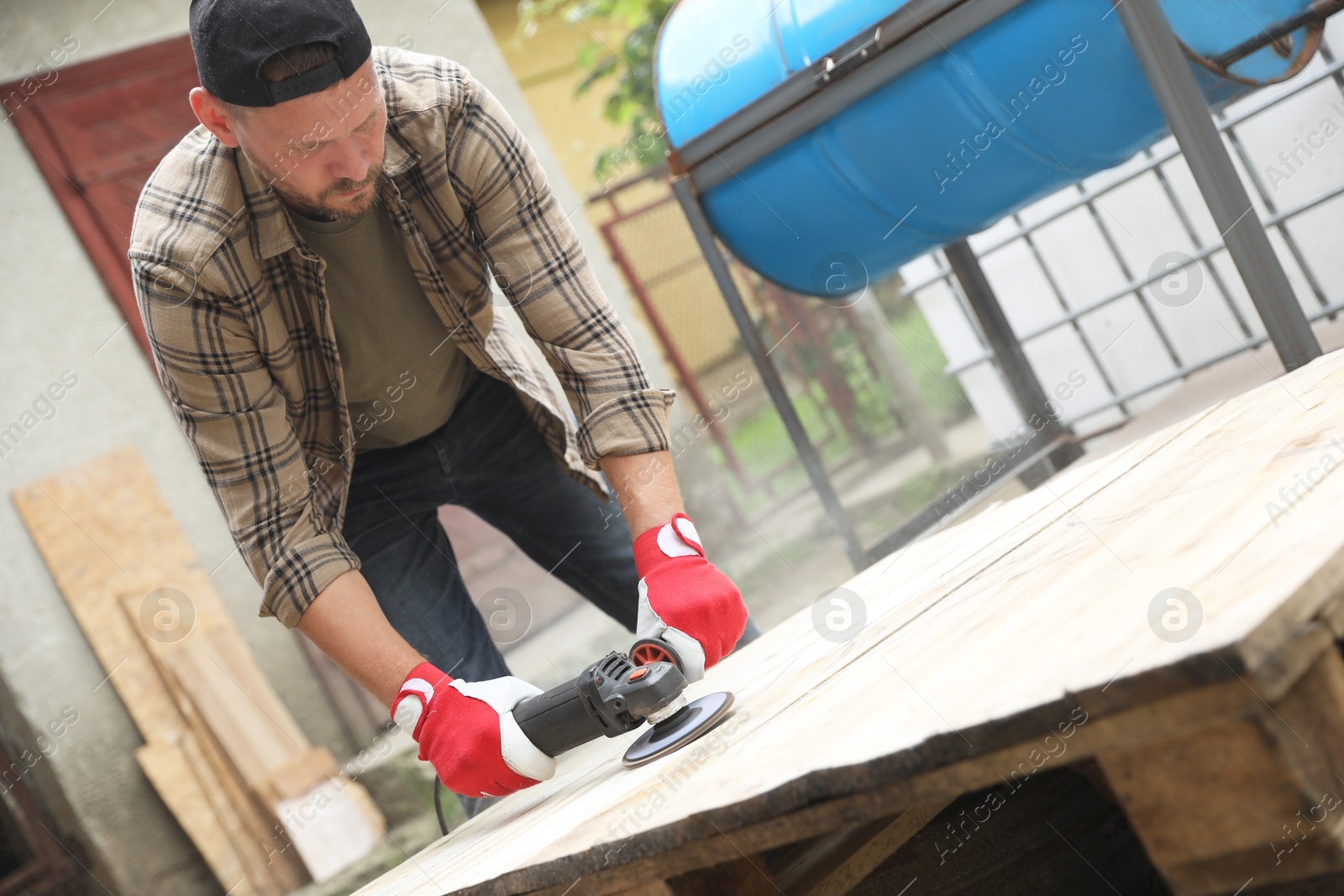 Photo of Man polishing wooden planks with angle grinder outdoors