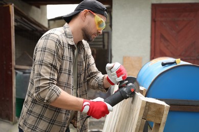 Photo of Man grinding wooden planks with angle grinder outdoors