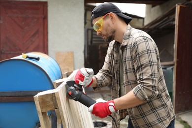 Man grinding wooden planks with angle grinder outdoors