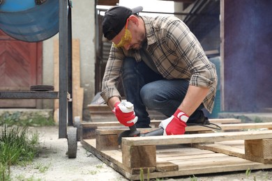 Photo of Man grinding wooden planks with angle grinder outdoors