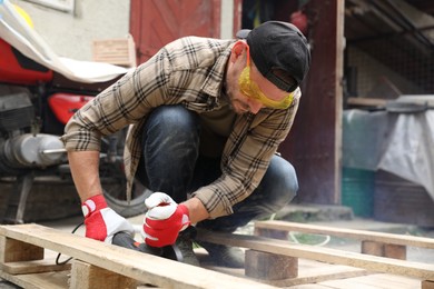 Photo of Man grinding wooden planks with angle grinder outdoors