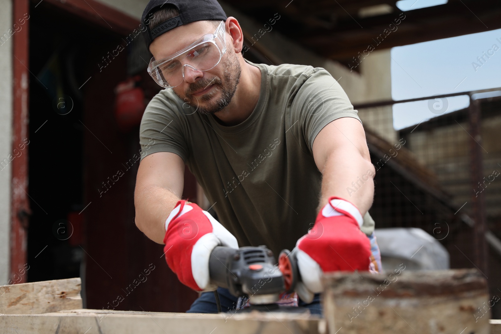 Photo of Man polishing wooden planks with angle grinder outdoors